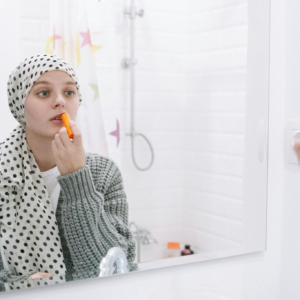 A woman in a headscarf applies lip balm, symbolizing strength and cancer awareness.