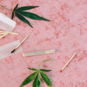Artistic flat lay of cannabis leaves and matches on a textured pink background.